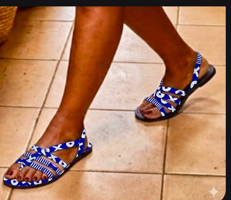 wardrobe with these stylish and comfortable flat sandals, as seen on a model in a sophisticated home setting. Featuring unique blue and white patterned straps and a natural tan sole, they are the perfect blend of casual elegance.  Ideal for pairing with everything from dresses to shorts for a chic summer look.